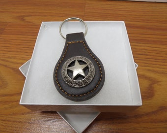 May include: A brown leather keychain with a silver five-pointed star in a circle design.