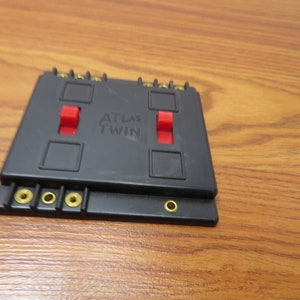 May include: Black Atlas Twin model railroad switch with two red toggle switches and gold-colored terminals.