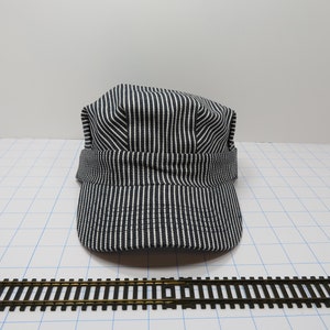May include: A black and white striped engineer's cap with a brim. The cap is made of a cotton fabric and has a classic design.
