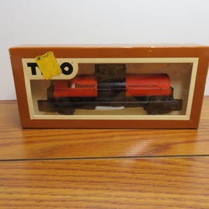 May include: A vintage toy train set in its original box. The train is red and black, with the word "Hooker" printed on the side. The box is brown with a clear plastic window, and a yellow tag is attached to the top.