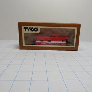 May include: A Tyco model train caboose in a brown box. The caboose is red and white with the text "ROCKY MOUNTAIN LINE". The box has the Tyco logo.