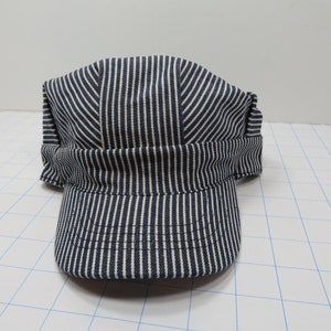 May include: A blue and white striped engineer's cap with a brim. The cap is made of a cotton fabric and has a classic design.