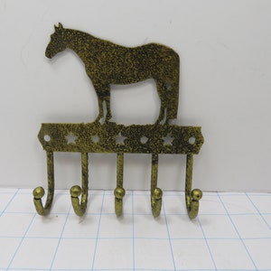 May include: Gold metal horse silhouette key holder with five hooks. The horse is standing on a base with stars.
