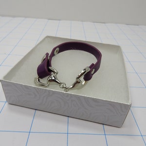 May include: A purple leather bracelet with a silver horse bit clasp. The bracelet is in a white gift box.