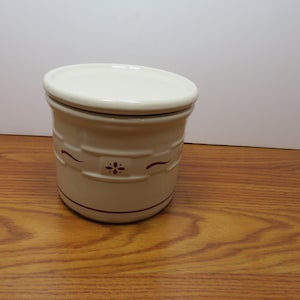 May include: A white ceramic canister with a red floral design and a matching lid. The canister has a red band around the top and bottom.