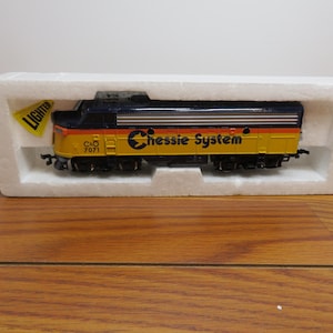 May include: A model train in a white foam container. The train is yellow, black, and orange with the words "Chessie System" and "C&O 7071" printed on the side. A yellow tag with the word "Lighter" is attached to the container.