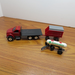 May include: A red toy truck with a black flatbed trailer, a red wagon with a gray metal top, and a white tank labeled "Anhydrous Ammonia".