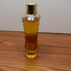 May include: A clear glass bottle with a gold cap filled with a yellow liquid. The bottle has a textured design and is sitting on a wooden surface.