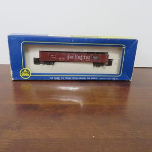 May include: A model train car in a blue box. The train car is red with the word "Burlington" printed on the side. The box has the text "The finest HO trains from around the world."