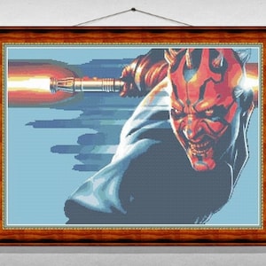 Puede incluir: Una obra de punto de cruz enmarcada que presenta un primer plano de Darth Maul, un Lord Sith de piel roja de Star Wars, con su sable de luz de doble hoja encendido. El fondo es un degradado azul y blanco.