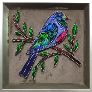 May include: A framed string art depiction of a blue bird on a brown branch with green leaves. The bird's body is crafted from blue, green, and pink threads, with silver accents. The artwork is set against a grey background.