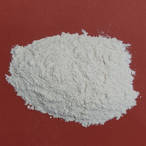 Może przedstawiać: Zbliżenie na stos białego proszku na czerwonej powierzchni. Proszek jest drobny i pylący, i wydaje się być rodzajem mąki lub skrobi.