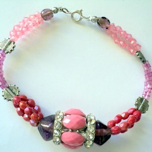 Peut inclure: Un bracelet en perles rose et rouge avec une grosse perle rose et violette au centre. Le bracelet est orné d'accents argentés et d'un fermoir argenté.