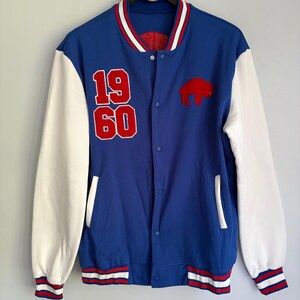 May include: A blue varsity jacket with white sleeves, featuring a red embroidered buffalo patch on the chest and the red numbers 19 and 60 stacked vertically. The jacket has a striped ribbed collar, cuffs, and hem, with a snap-button front closure.