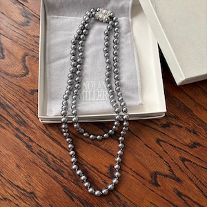 May include: A two-strand gray pearl necklace with a rhinestone clasp, presented in a white box with a gray satin lining. The necklace is from the "Nolan Miller" collection.