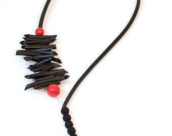 May include: A black necklace with a long strand of black beads and a cluster of black tube-like beads with two red beads at the top.