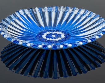 May include: A blue and white glass bowl with a decorative pattern of stripes and circles. The bowl is made of glass and has a shiny finish.