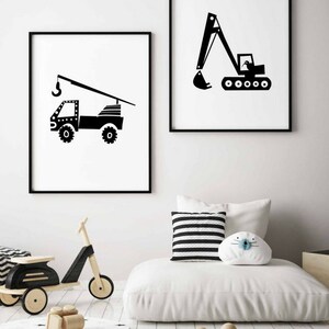 May include: Two black and white illustrations of construction vehicles, a crane truck and an excavator, framed in black frames and hung on a white wall.