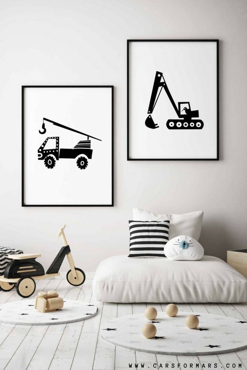 May include: Two black and white illustrations of construction vehicles, a crane truck and an excavator, framed in black frames and hung on a white wall.