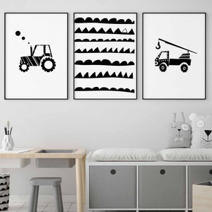 May include: Three black and white framed prints featuring a tractor, a truck with a crane, and a geometric pattern of waves and triangles. The prints are hanging on a white wall above a wooden desk and a grey storage bench with cushions.