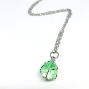 May include: A silver chain necklace with a green and white stone pendant. The stone is encased in a silver wire cage.
