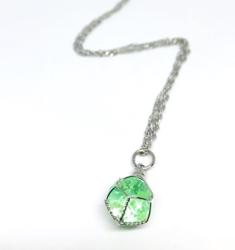 May include: A silver chain necklace with a green and white stone pendant. The stone is encased in a silver wire cage.