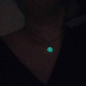 May include: A close-up of a person wearing a black shirt with a glowing green pendant necklace.