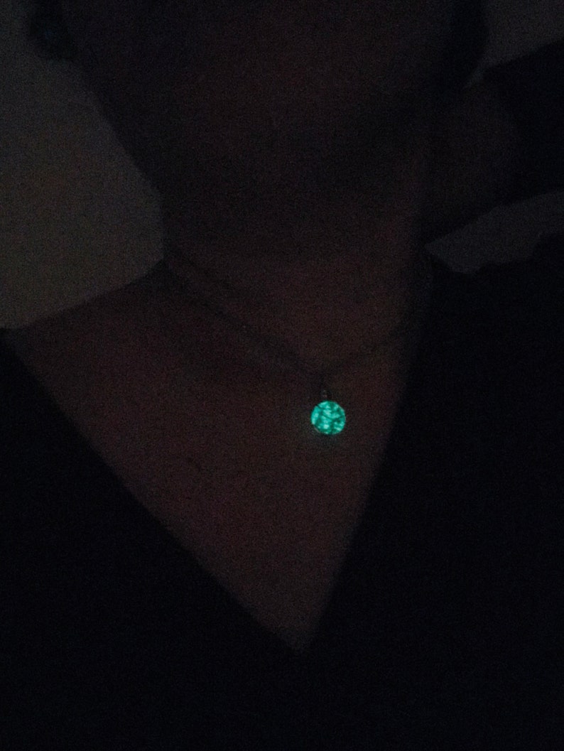 May include: A close-up of a person wearing a black shirt with a glowing green pendant necklace.