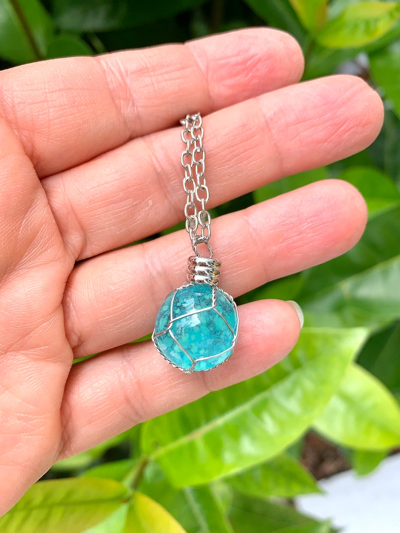 May include: A turquoise gemstone pendant necklace with a silver chain. The gemstone is encased in a silver wire cage.