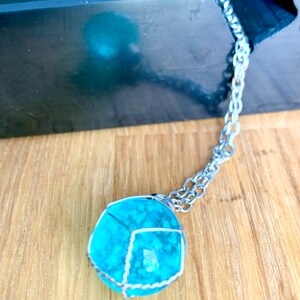 May include: A turquoise gemstone pendant necklace with a silver chain. The gemstone is encased in a silver wire cage.