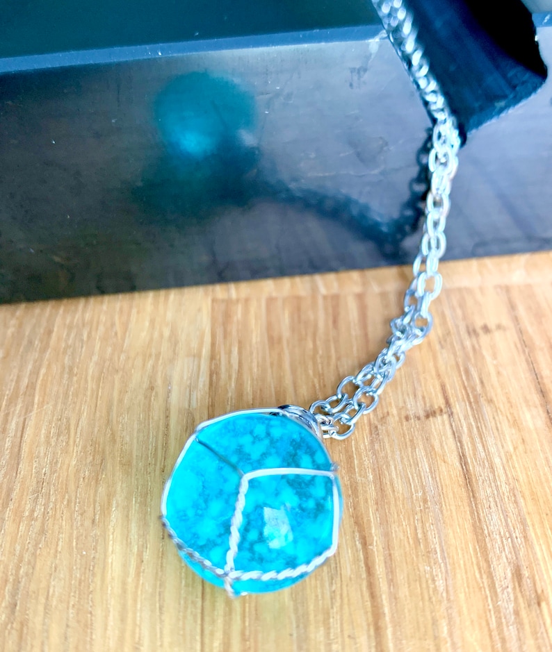May include: A turquoise gemstone pendant necklace with a silver chain. The gemstone is encased in a silver wire cage.