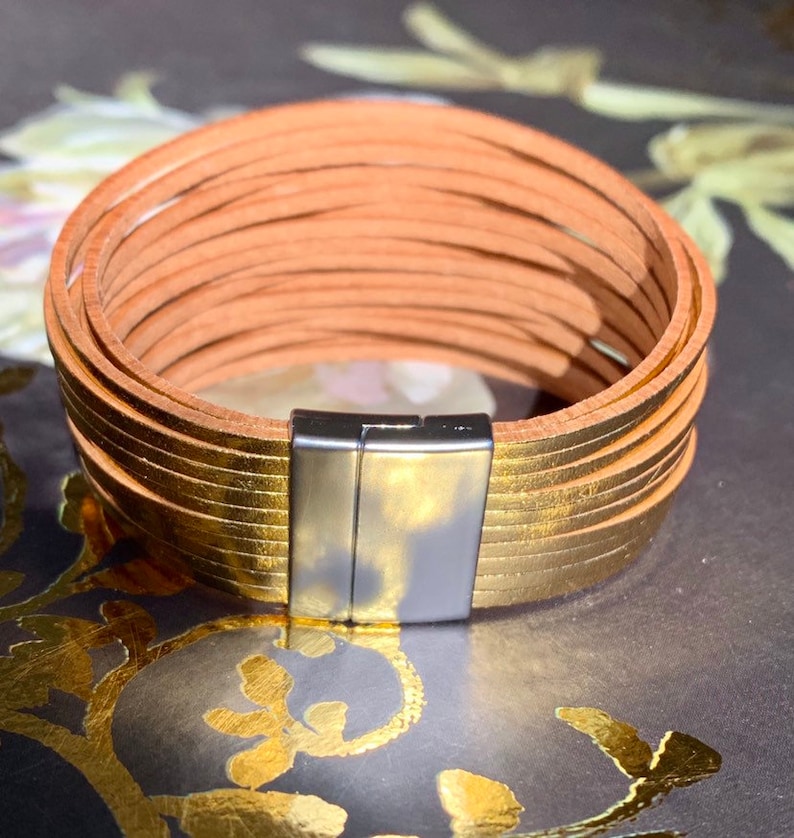 May include: A multi-strand bracelet with a magnetic clasp. The bracelet features multiple strands of tan leather and gold-colored leather. The clasp is silver-colored. The bracelet is approximately 7 inches in circumference.