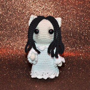 May include: A crocheted doll with long black hair and a white dress. The doll has large black eyes and a sweet expression.