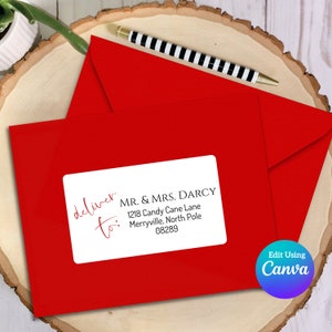 Puede incluir: Una etiqueta de dirección blanca con el texto "deliver to:" en escritura cursiva roja. El texto "MR. & MRS. DARCY" está en negro, seguido de la dirección "1218 Candy Cane Lane, Merryville, North Pole 08289".