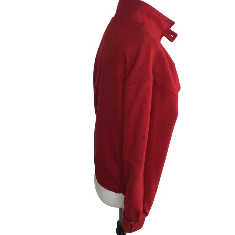 May include: A red wool jacket with a high collar and a zipper closure. The jacket has a long sleeve and a relaxed fit.