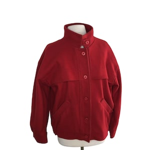 May include: A red wool jacket with a stand-up collar, a button-up front, and two pockets.