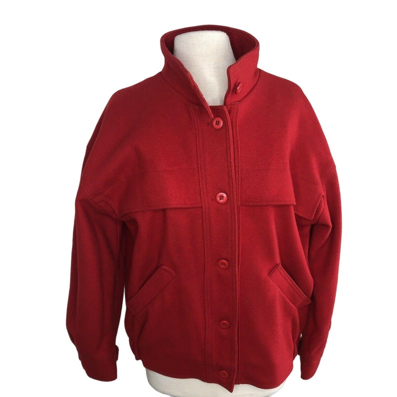 May include: A red wool jacket with a button-up front and two pockets. The jacket has a stand-up collar and long sleeves.