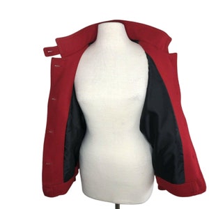 May include: A red wool coat with a black lining. The coat is open and the lining is visible. The coat has a collar and buttons.
