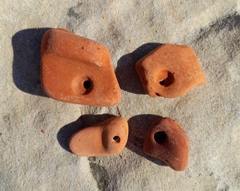 May include: Four terracotta-colored climbing holds, each with a unique shape and a hole for attaching to a climbing wall. The holds are arranged on a light gray surface.