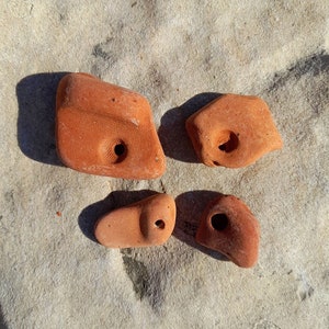 Può includere: Quattro prese da arrampicata in terracotta, ognuna con una forma unica e un foro per il fissaggio a una parete da arrampicata. Le prese sono disposte su una superficie grigio chiaro.