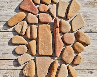 May include: A collection of various smooth, weathered stones in shades of tan, beige, and terracotta. The stones are arranged in a loose, rounded cluster, displaying diverse shapes including rectangular, triangular, and oval forms with natural textures.