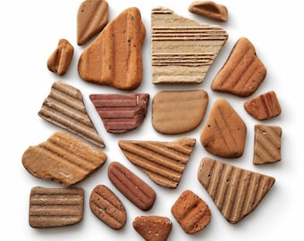 May include: A collection of various terracotta-colored ceramic shards and fragments. The pieces feature diverse shapes, including triangular, rectangular, and irregular forms, with some displaying linear grooved textures and others smooth surfaces.