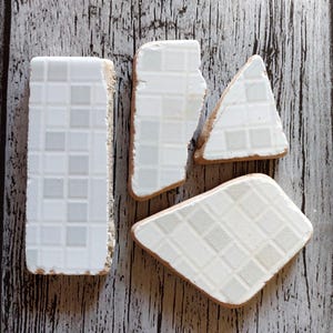 May include: Four white ceramic tiles with a grid pattern. The tiles are broken and have irregular edges.