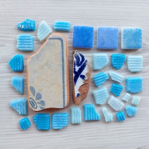 Può includere: Una collezione di piastrelle in ceramica blu e bianca con un motivo floreale. Le piastrelle sono disposte in un motivo a griglia su una superficie di legno bianco.