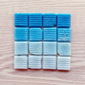 Puede incluir: Un conjunto de 12 pequeñas baldosas de mosaico cuadradas, azules y azul claro. Las baldosas tienen una superficie texturizada y estriada.