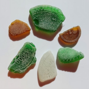 Puede incluir: Seis piezas de vidrio de mar en varias formas y colores, incluyendo verde, marrón y blanco. Algunas piezas tienen texto en ellas, incluyendo "Good" y "5".