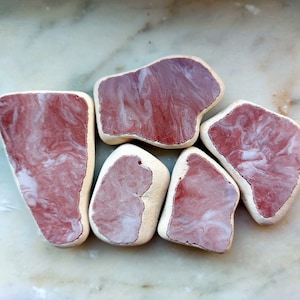 May include: Five irregularly shaped, pink and white marbled resin pieces. The pieces are smooth and have a polished finish.