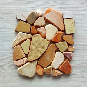 Pode incluir: Uma coleção de pequenos azulejos de terracota de forma irregular em tons de marrom, laranja e amarelo. Os azulejos estão dispostos em um padrão aleatório.