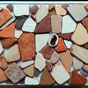 May include: A collection of small, irregular shaped, ceramic tiles in various shades of brown, orange, white, and beige. The tiles are arranged in a mosaic pattern.