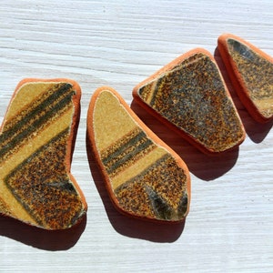 Könnte beinhalten: Vier Keramikfliesen mit einem geometrischen Muster in Gelb, Braun und Grün. Die Fliesen sind versetzt angeordnet.